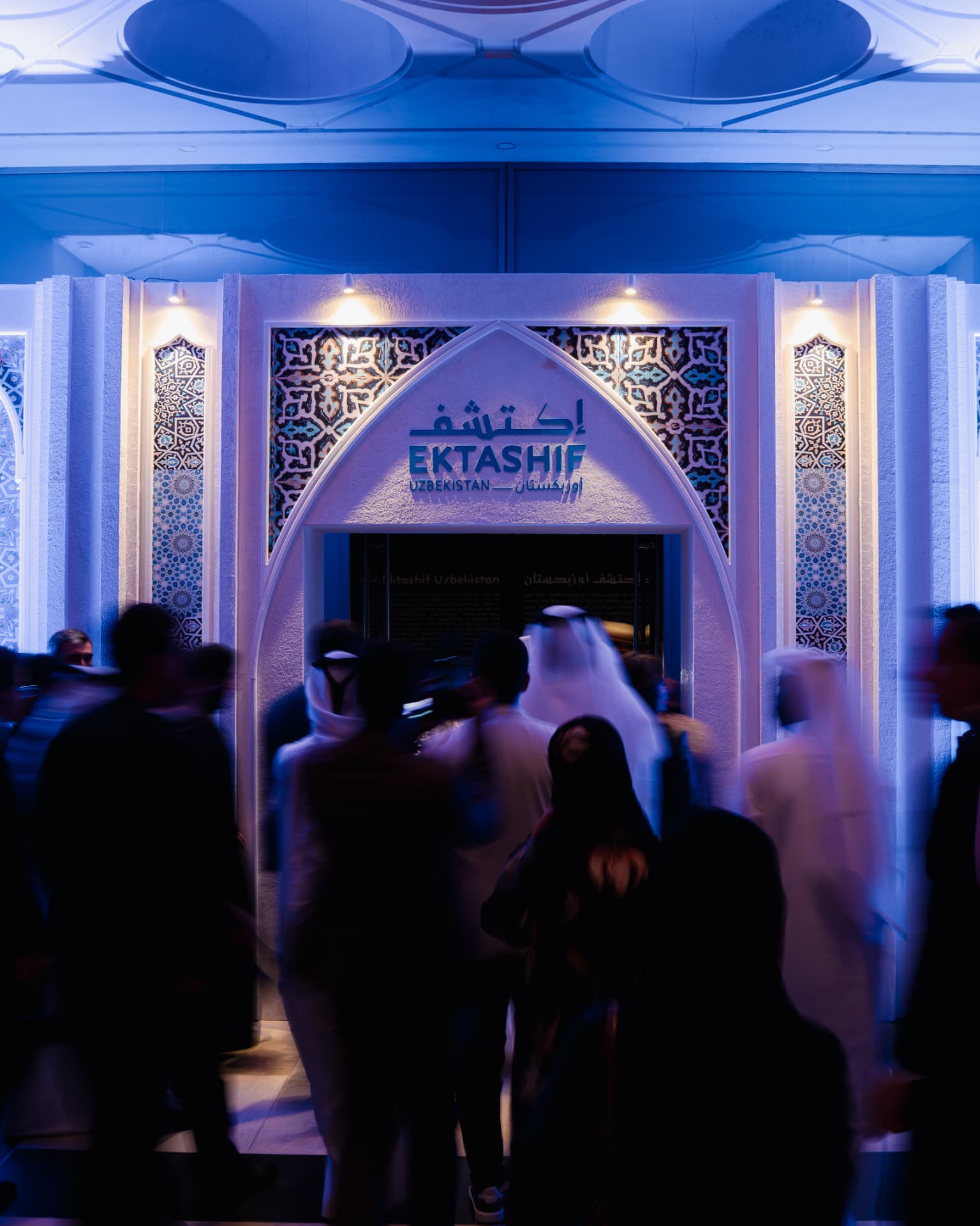 Illuminated entrance to the Ektashif Uzbekistan exhibition with visitors walking in