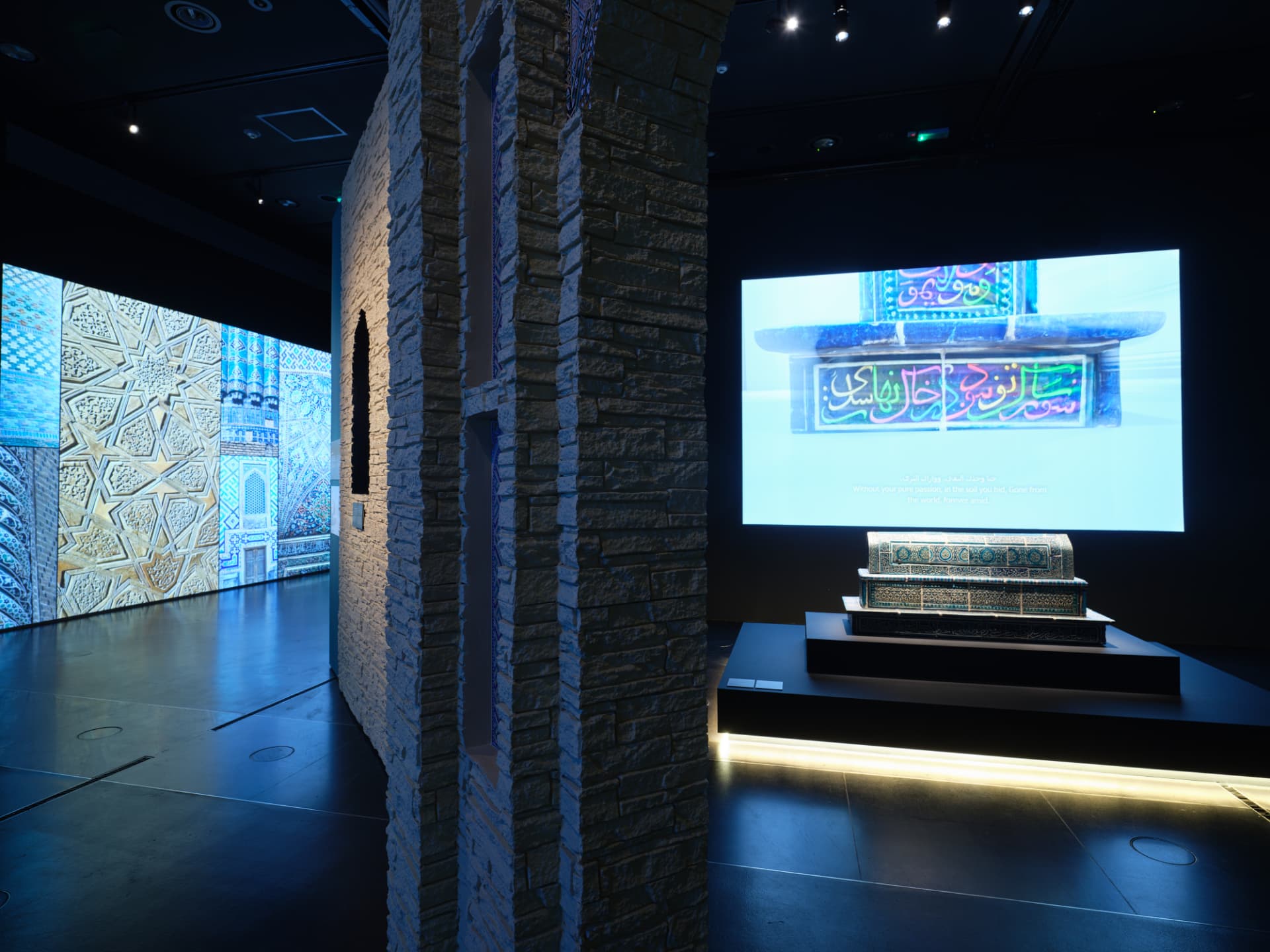 A blue-lit installation projecting Islamic geometric patterns over stonework and a display case