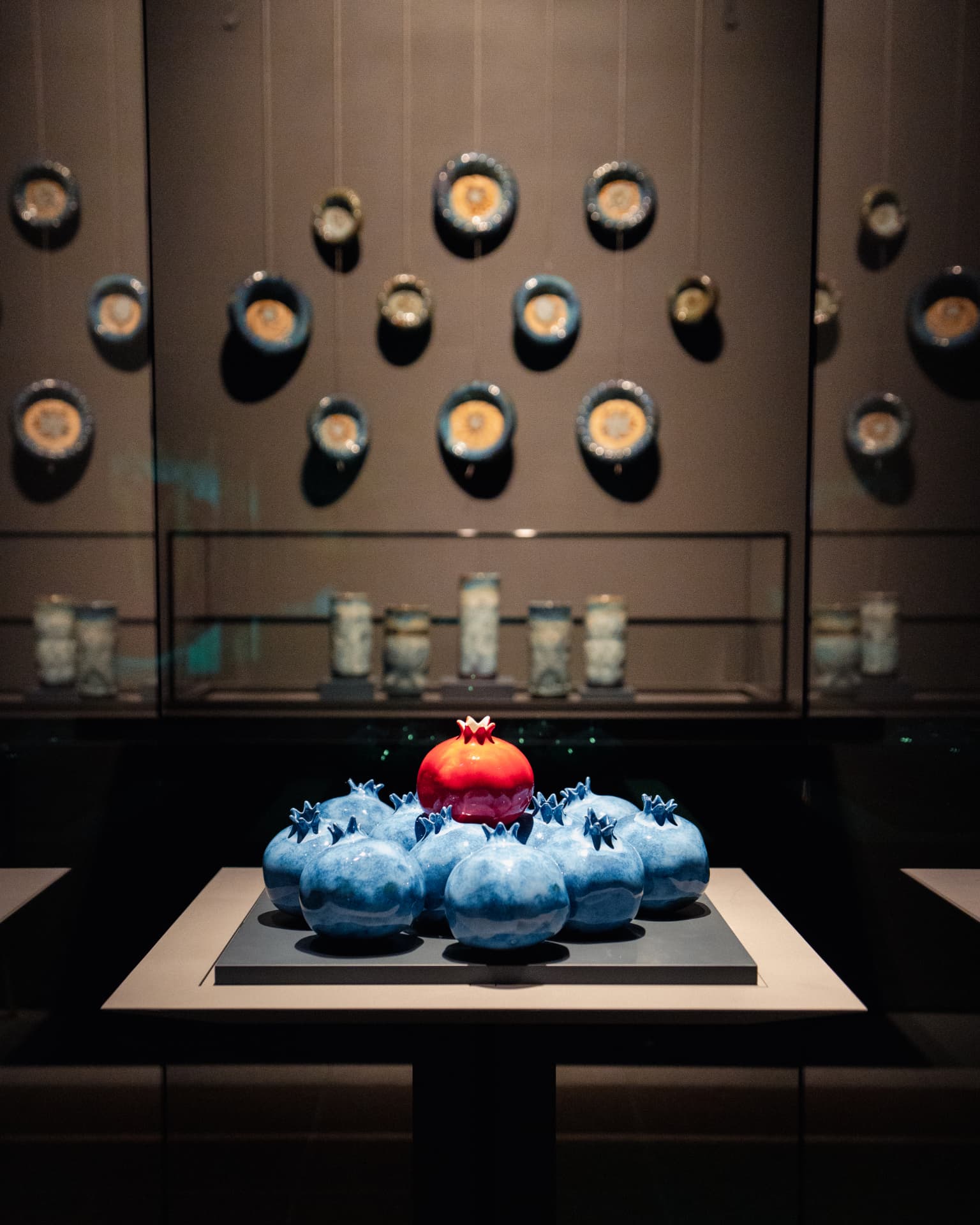 A blue and red pomegranate sculpture beneath mounted circular objects in the exhibition