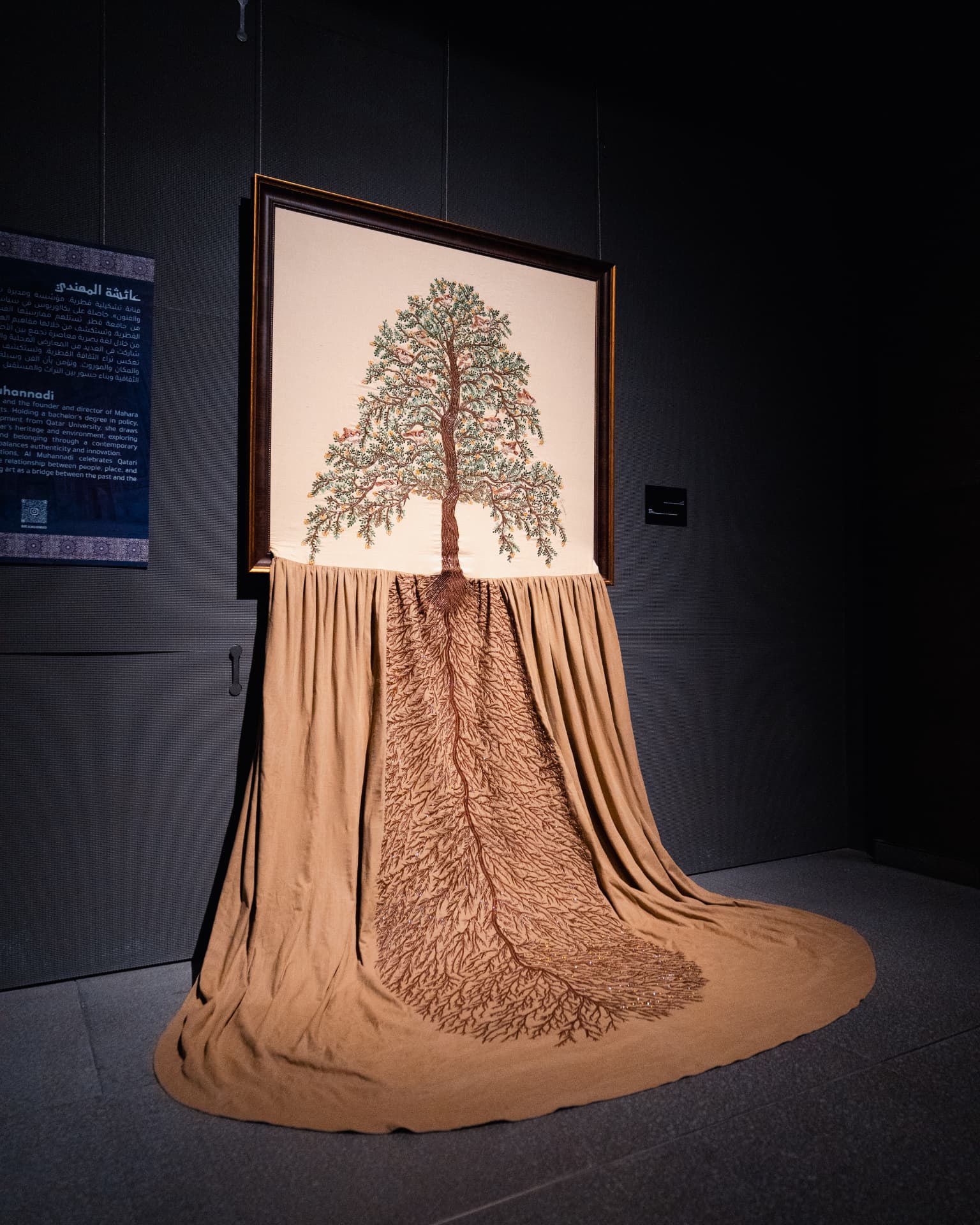 A framed embroidered tree artwork with roots extending onto draped fabric