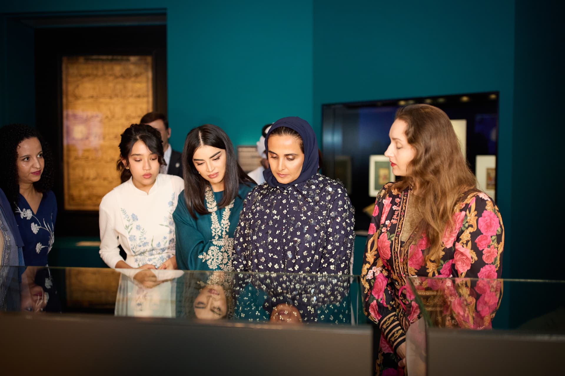 Visitors gathered around an exhibition display in a teal-walled gallery